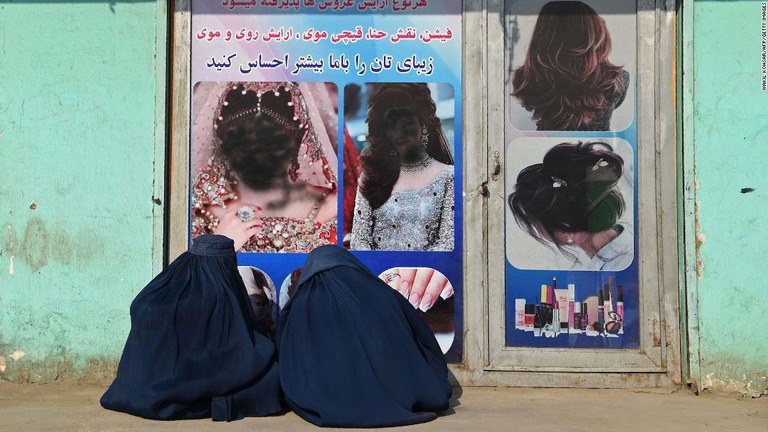 美容院の前に座るアフガニスタンの女性たち。掲示された女性の顔写真がスプレーで汚されている＝２０２１年１２月１３日、アフガニスタン東部ジャララバード/Wakil Kohsar/AFP/Getty Images