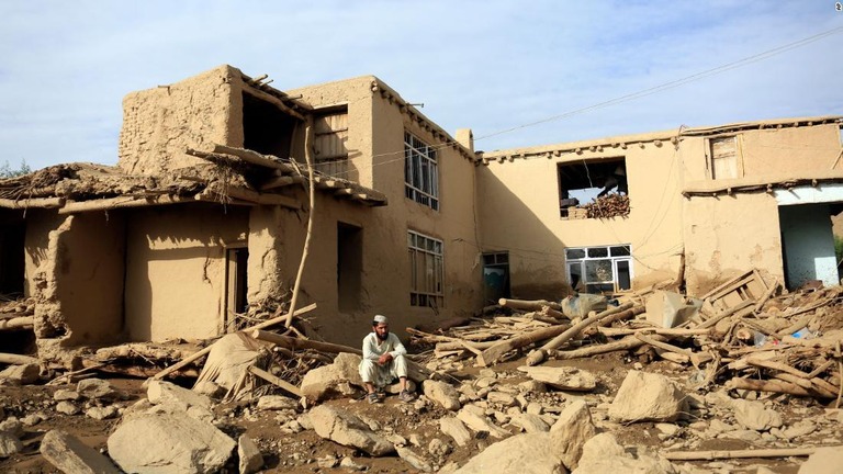 損壊した建物の前に座る男性＝２３日、アフガニスタン・ワルダク州/AP