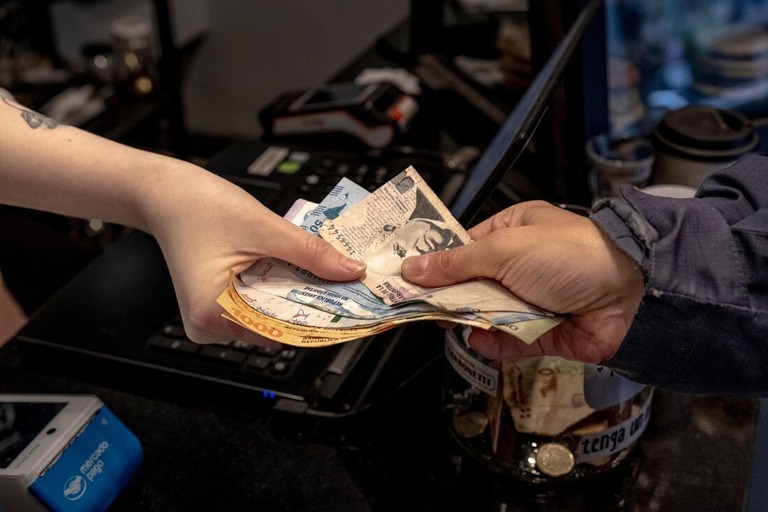 店舗でペソの紙幣を受け取る従業員＝９月２６日、アルゼンチン・ブエノスアイレス/Erica Canepa/Bloomberg/Getty Images