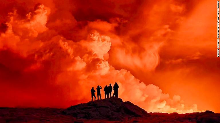溶岩が夜空をオレンジ色に染める中、立ち上る煙を眺める地元住民/Kristin Elisabet Gunnarsdottir/AFP/Getty Images