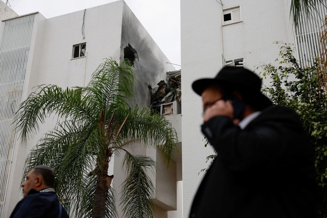 ロケット弾で損傷した建物の近くを歩く人々＝１２月５日、イスラエル・アシュケロン/Amir Cohen/Reuters