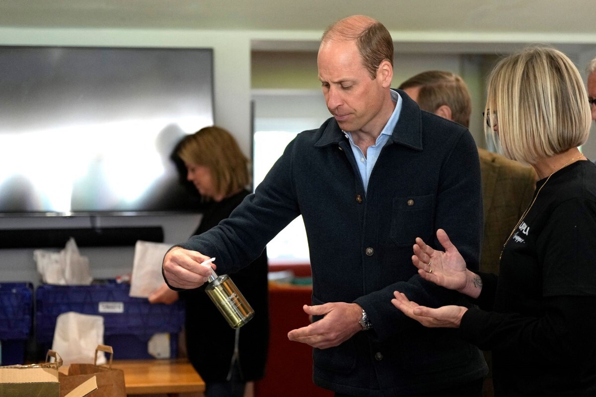 慈善事業の担当者から品物の説明を受ける英ウィリアム王子/Alastair Grant/Reuters